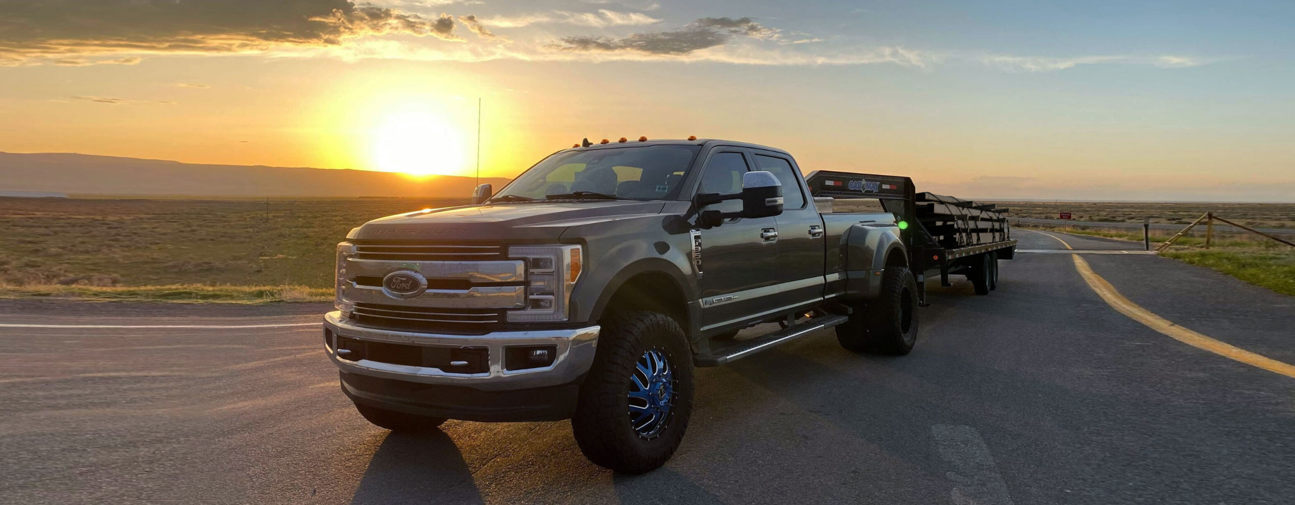 Black pickup truck pulling flatbed trailer with metal piping over USA highway