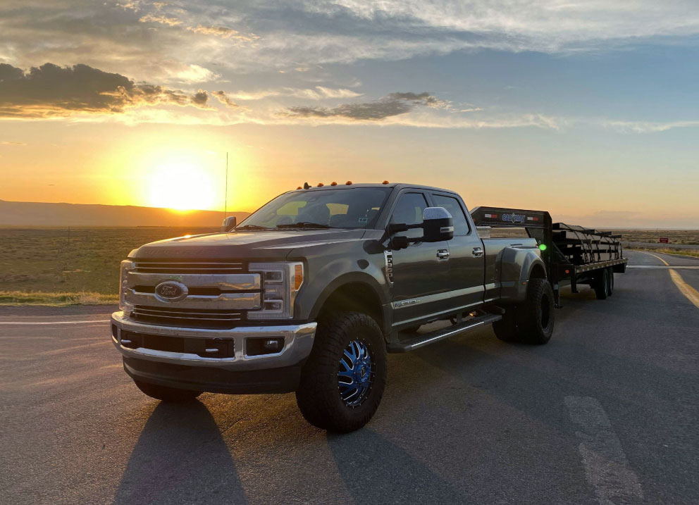 Black pickup truck pulling flatbed trailer with metal piping over USA highway