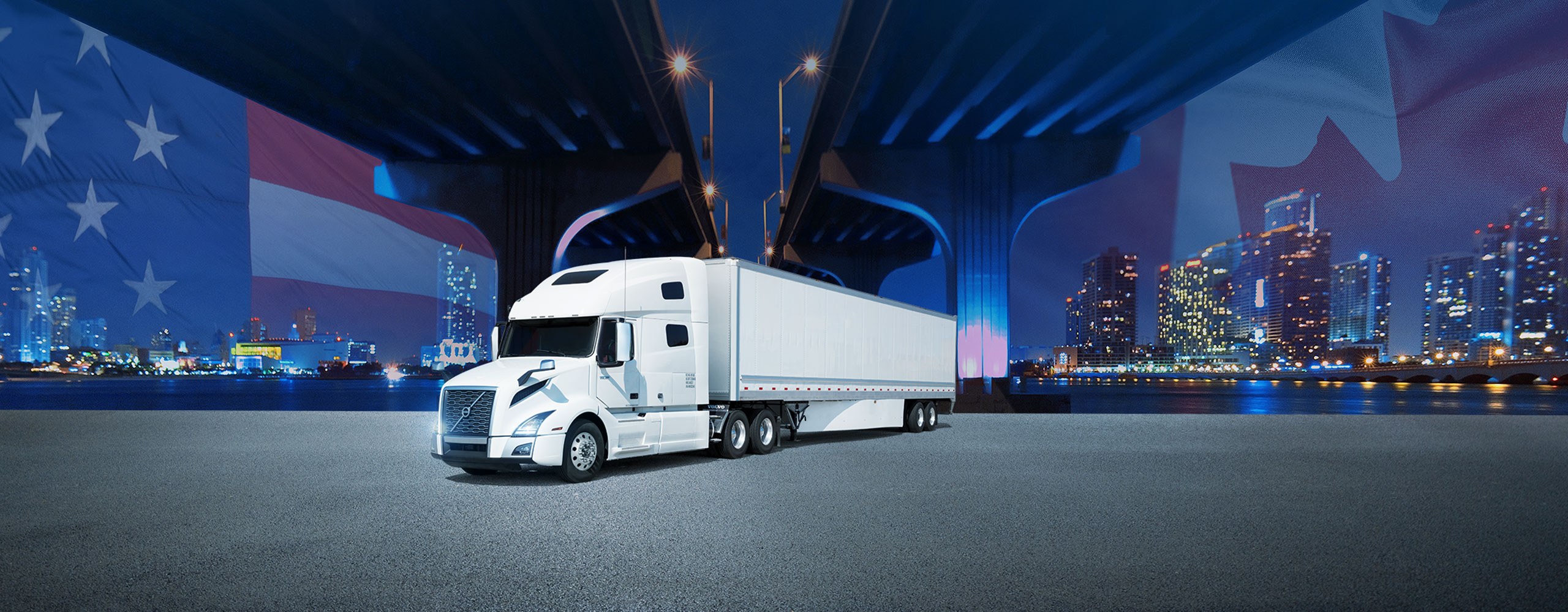 White tractor trailer parked under international bridge with Canada and USA flags and cityscapes in the background