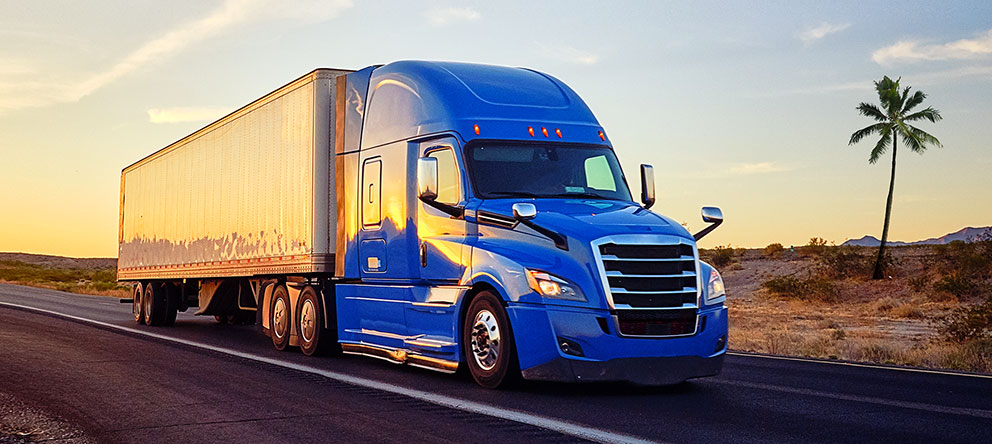 Blue tractor pulling white trailer with truckload shipment across USA highway