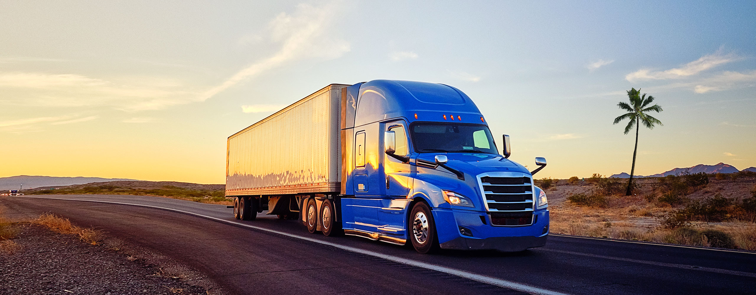 Blue tractor pulling white trailer with truckload shipment across USA highway